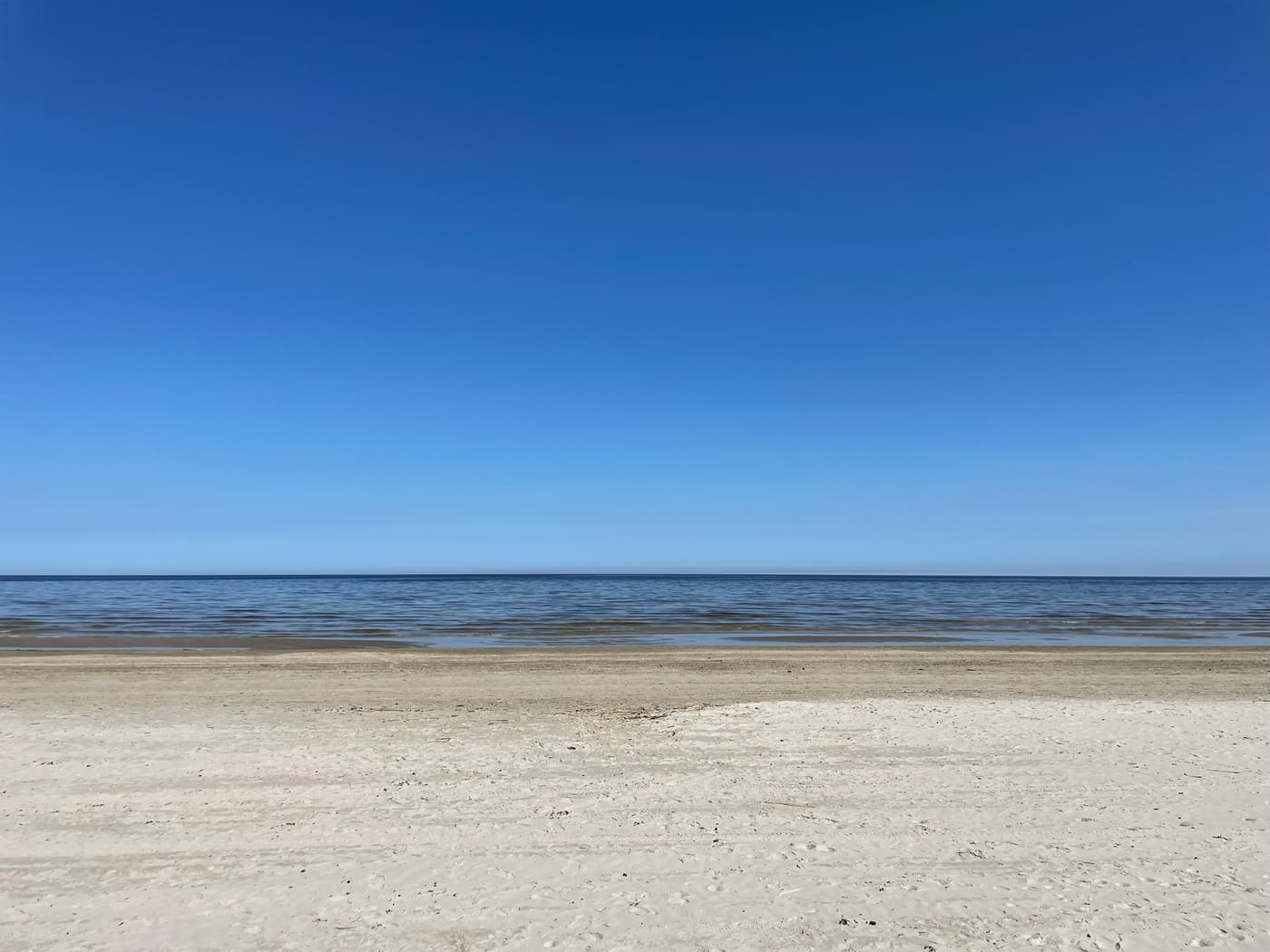 The wide sandy beach and calm Gulf of Riga at Jūrmala under a clear blue sky