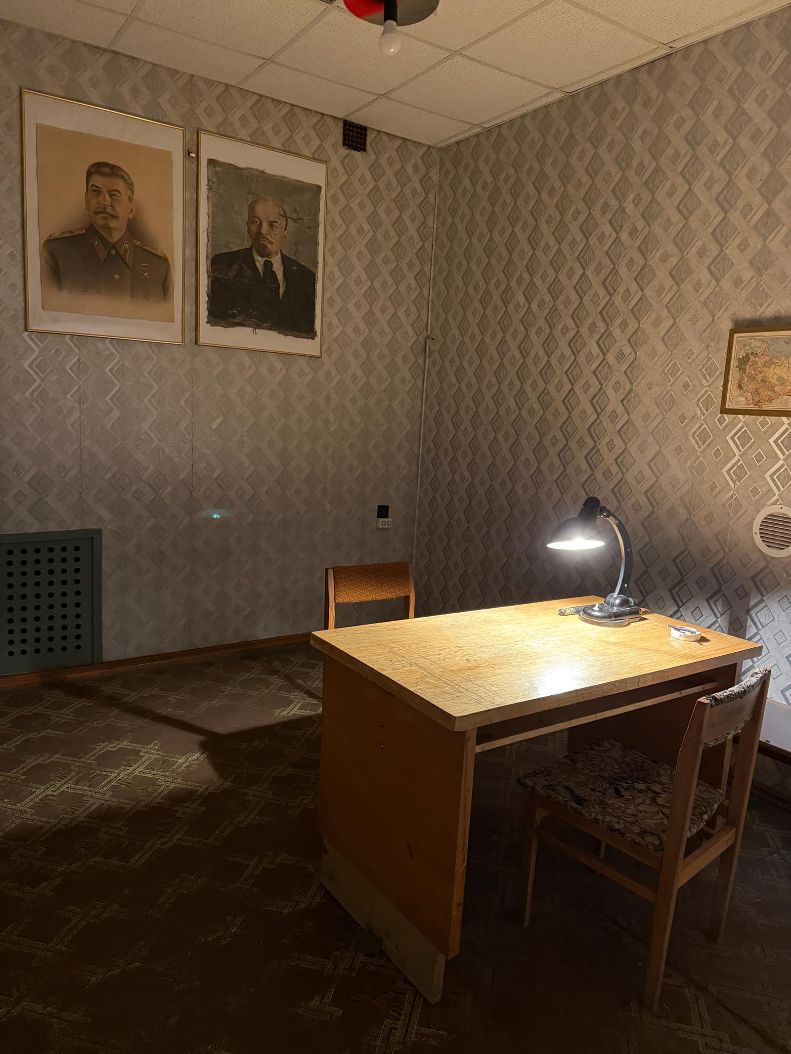 Der Verhörraum: ein Schreibtisch, eine Lampe, ein Schlagstock und ein Spiegel, der eine Beobachtungskammer verbirgt.