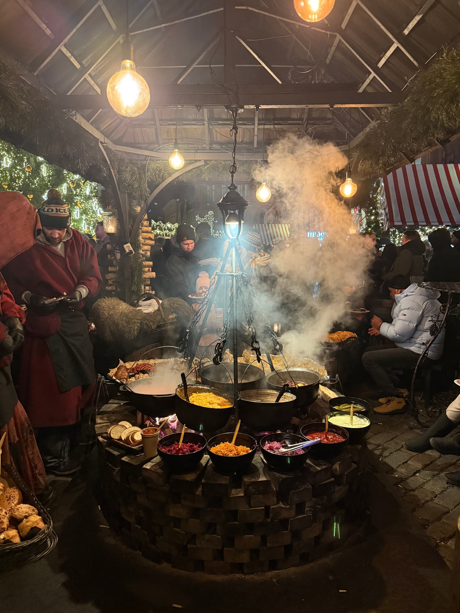 A central fire pit with cauldrons of stew and bowls of salads and pickles at the Riga Christmas market