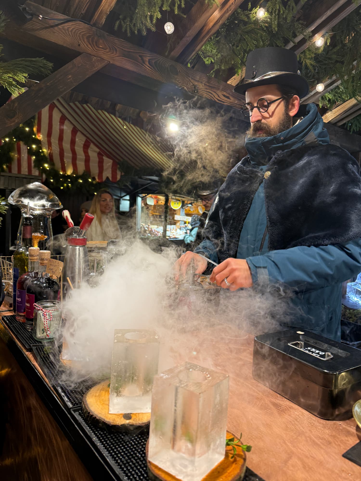 A costumed bartender mixing a cocktail served in a carved ice glass at the Riga Christmas market